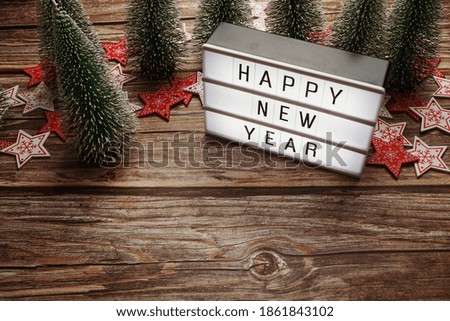 Happy New Year word in light box with Christmas tree decoration on wooden background