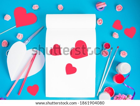 Valentine's day background. Notepad with red hearts, jewelry, pencils and paints on a blue background, top view. Free space for text