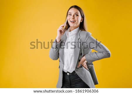 Young woman in suit using a smartphone on yellow background