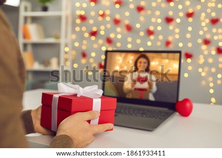 Video call on Saint Valentine's Day. Couple sending each other love and showing presents on virtual date. Closeup of man's hands holding gift box. Shimmering yellow lights, soft focus, selective focus Royalty-Free Stock Photo #1861933411