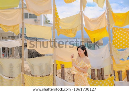 Asian woman eating some ice cream with yellow Dress standing front of the yellow fabric background at the beach in the middle of sun shine in summer