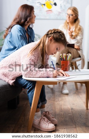 little girl patient drawing picture while visiting psychologist with mother