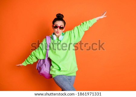 Photo of dancing sweet young woman wear green hoodie schoolbag glasses showing plane isolated vivid orange color background