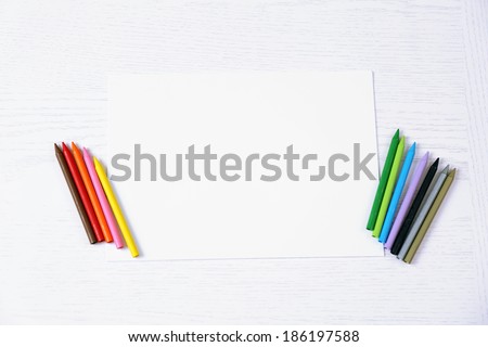 Colored pencils and blank paper sheet on wooden table