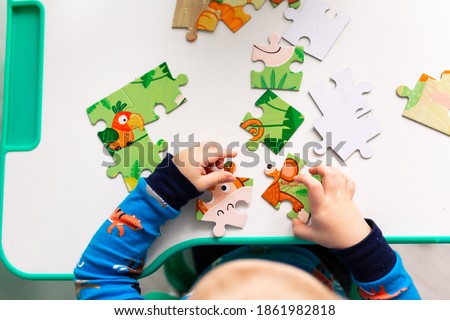 Baby boy solving jigsaw puzzle on the desk, focusing on the hands