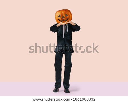 Man  with Halloween pumpkin in black costume, minimal holiday concept on a pastel background 