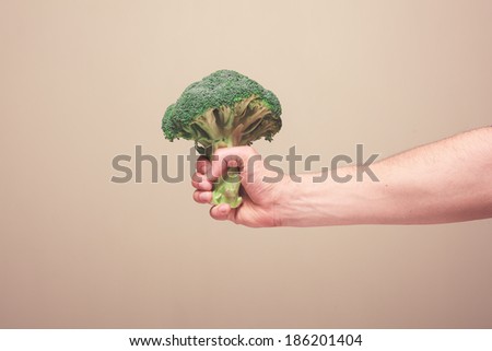 The hand of a young man is holding a floret of broccoli