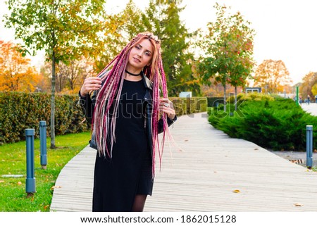 beautiful model with long dreadlocks and pigtails in black clothes walks in the park. Portrait of an attractive young woman outdoors, retouched