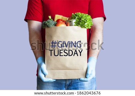 Volunteer in medical gloves holds paper grocery bag with inscription Giving tuesday on blue background. Charity, help and donation concept. Royalty-Free Stock Photo #1862043676
