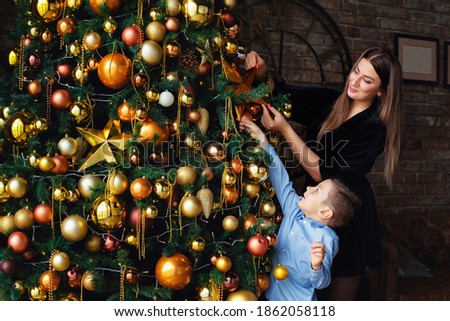 Mother and son decorate the Christmas tree with Golden balls and a star. Christmas with family.
