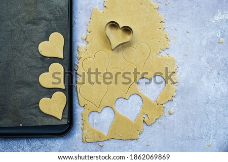 High angle close up of heart-shaped cookies cut out of cookie dough.