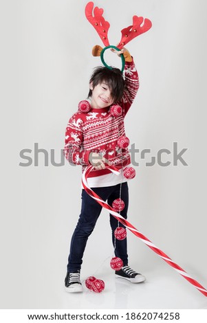 Hispanic boy dressed in a Christmas sweater and a giant cane on a white background