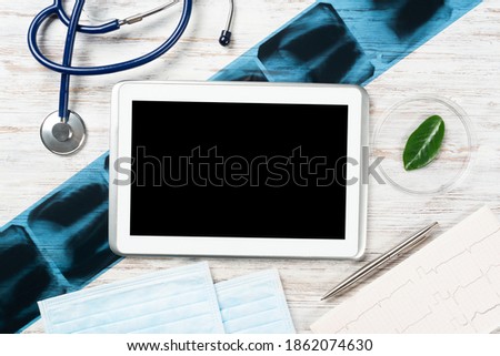 Mock up of doctors desktop with medical supplies. Tablet computer, x-ray image, stethoscope and cardiogram lies on wooden desk. Professional healthcare technology. Medical consultation and treatment.