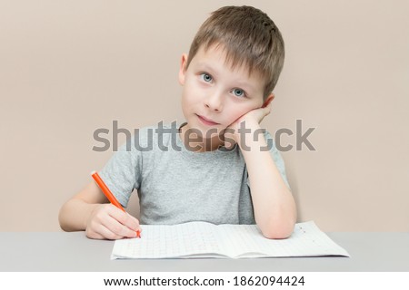 the boy preschool sits at a table with a pen and notebook. The child learns to write. The idea is preparing for school, completing tasks. Horizontal photo.