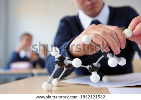 A close up shot of a student's hand in school uniform assembling an atom model at a desk. Royalty-Free Stock Photo #1862121562