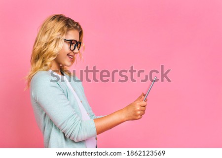 Portrait of adorable blonde kid using digital tablet device, isolated over pink background.