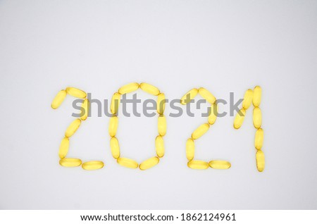 Number 2021 of yellow transparent omega 3 capsules and stars on a white background. Creative concept of a healthy lifestyle and proper nutrition. Christmas medical flat lay.
