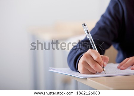 A close up shot of a student's hand writing exam at his desk. Royalty-Free Stock Photo #1862126080