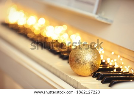 Beautiful golden bauble and fairy lights on piano keys, space for text. Christmas music