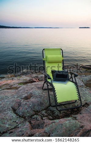 Laptop on lawn chair near remote river