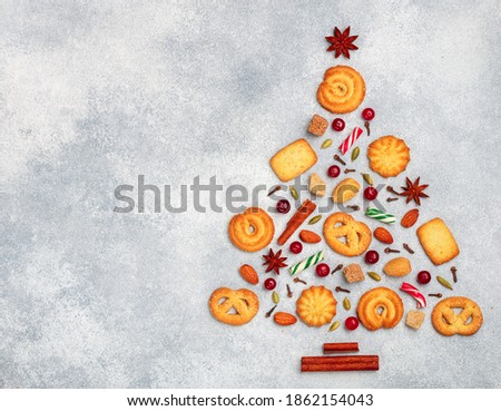 Culinary background of sugar cookies, almonds and spices in the form of a Christmas tree. Crunchy biscuits, cinnamon, cardamom, cloves, star anise, cranberries and caramel on a grey concrete surface
