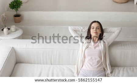 Happy satisfied millennial woman owner renter of new apartment. Female having rest sitting in comfortable pose on sofa at living room with modern interior design, copy space. Royalty-Free Stock Photo #1862155147