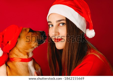 Blue-eyed girl and a puppy in Santa Claus hats on a red background. Christmas.