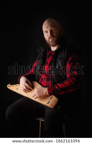 Portrait of a bearded man with a Kantele, a national Finnish and Karelian musical instrument, also known as the psaltery (gusli) in Russia and as the kankles, kokle, and Kannel in the Baltic States. Royalty-Free Stock Photo #1862161096