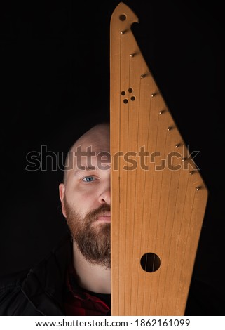 Bearded man hides his face behind Kantele, a national Finnish and Karelian musical instrument, also known as the psaltery (gusli) in Russia and as the kankles, kokle, and Kannel in the Baltic States. Royalty-Free Stock Photo #1862161099