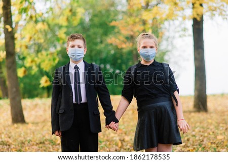 Schoolchildren, boy and girl in medical masks walk in the city park.