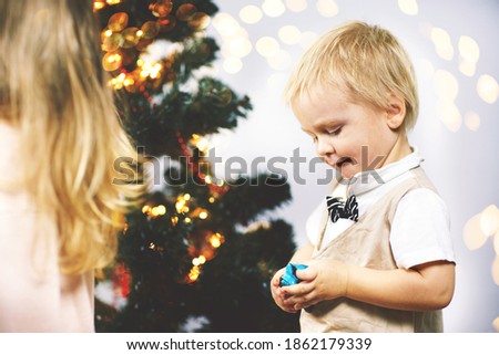 On Christmas night a little boy in a suit with a butterfly stands at the Christmas tree and unwraps a candy