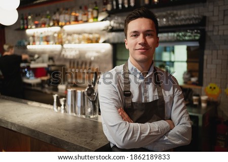 portrait of a staff member waiter in a restaurant cafe bistro. a young man of European appearance is waiting for new satisfied customers for dinner. professional work wear apron and shirt Royalty-Free Stock Photo #1862189833