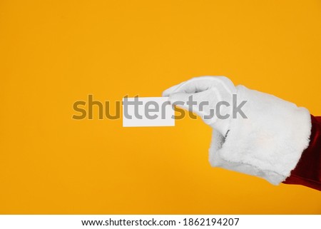 Santa Claus holding blank card on yellow background, closeup of hand. Space for text