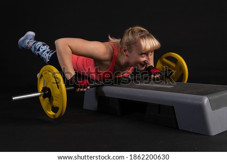Fitness girl on a step platform with a barbell with dumbbells. Going in for sports on a black background Joyful looking at the camera