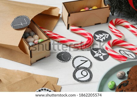 Paper bag and treats on white wooden table, closeup. Creating advent calendar
