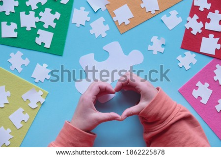 Hands show heart sign. Flat lay, top view on creative arrangement. Jigsaw puzzle elements and multicolor felt sheets on blue background.