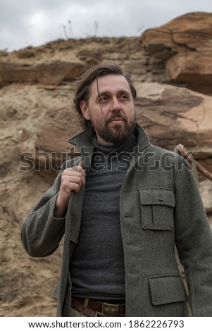 Brutal man in a pea jacket on the background of rocks