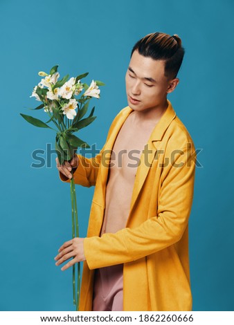 Side view of cute Asian guy with a bouquet of flowers on a blue background.