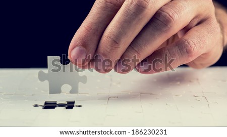 Close up of the hand of a man placing the last piece in place in a jigsaw puzzle conceptual of problem solving, finding a solution and meeting a challenge. Royalty-Free Stock Photo #186230231