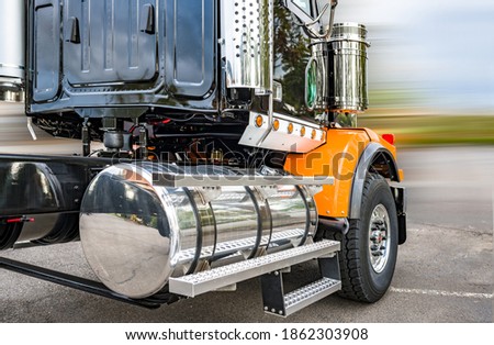 Powerful shiny big rig semi truck tractor in black and orange with polisher aluminum fuel tanks and steps and another accessories ready to go for industrial heavy freight 