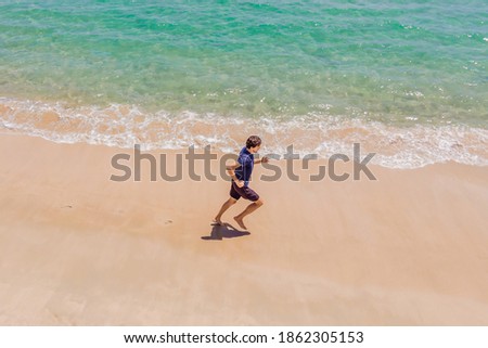 Runner running on beach by the ocean - view from above. Man athlete training cardio jogging doing morning workout. Hero aerial drone view shot, lots of copy space