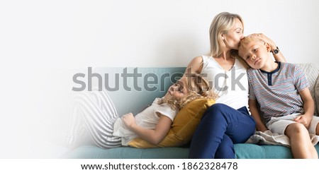 Blonde mom kissing her son's head and relaxing with daughter on the couch design space
