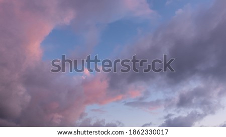 Evening sky. Against a blue background, beautiful pink and lilac cumulus clouds are illuminated by the setting sun. Full screen.