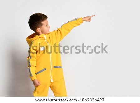portrait of cute smiling boy wearing warm overalls, showing to the side, isolated on white background. Child standing with hand outstretched above copy space. Sports kids fashion