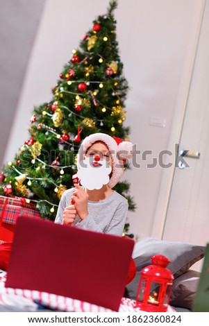Boy having fun with wear holidays decor using online communitation by laptop. Distance Christmas party. Social distancing