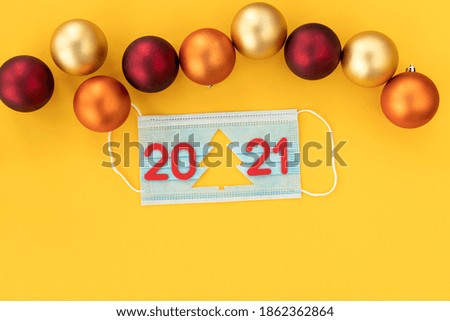 Medical mask with cut-out silhouette of Christmas tree and numbers 2021 with Christmas balls on a yellow background. New Year 2021 is coming. New Year concept, coronavirus concept. Copy space.