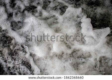 Close up view of rushing river water on high speed against river rocks creating foamy air bubbly water splash
