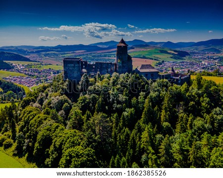 Aerial picture of Stara Lubovna Castle, Slovakia, medieval castle on a small hill surrounded by a green forest on summer sunny day, beautiful blue sky with clouds, Tatra Mountains in the background