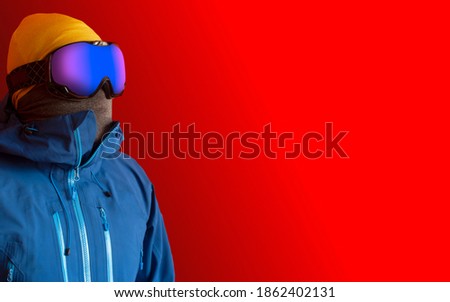 A man in spherical ski goggles looking ahead. Winter sport fashion isolated on a vivid red background with copy sapce on the right. Royalty-Free Stock Photo #1862402131