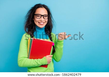Photo of happy brown haired pigtails young woman point thumb empty space old notebooks isolated on blue color background